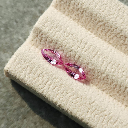 Two pink marquise sapphires seen from an oblique angle on the tilted cream display pad.
