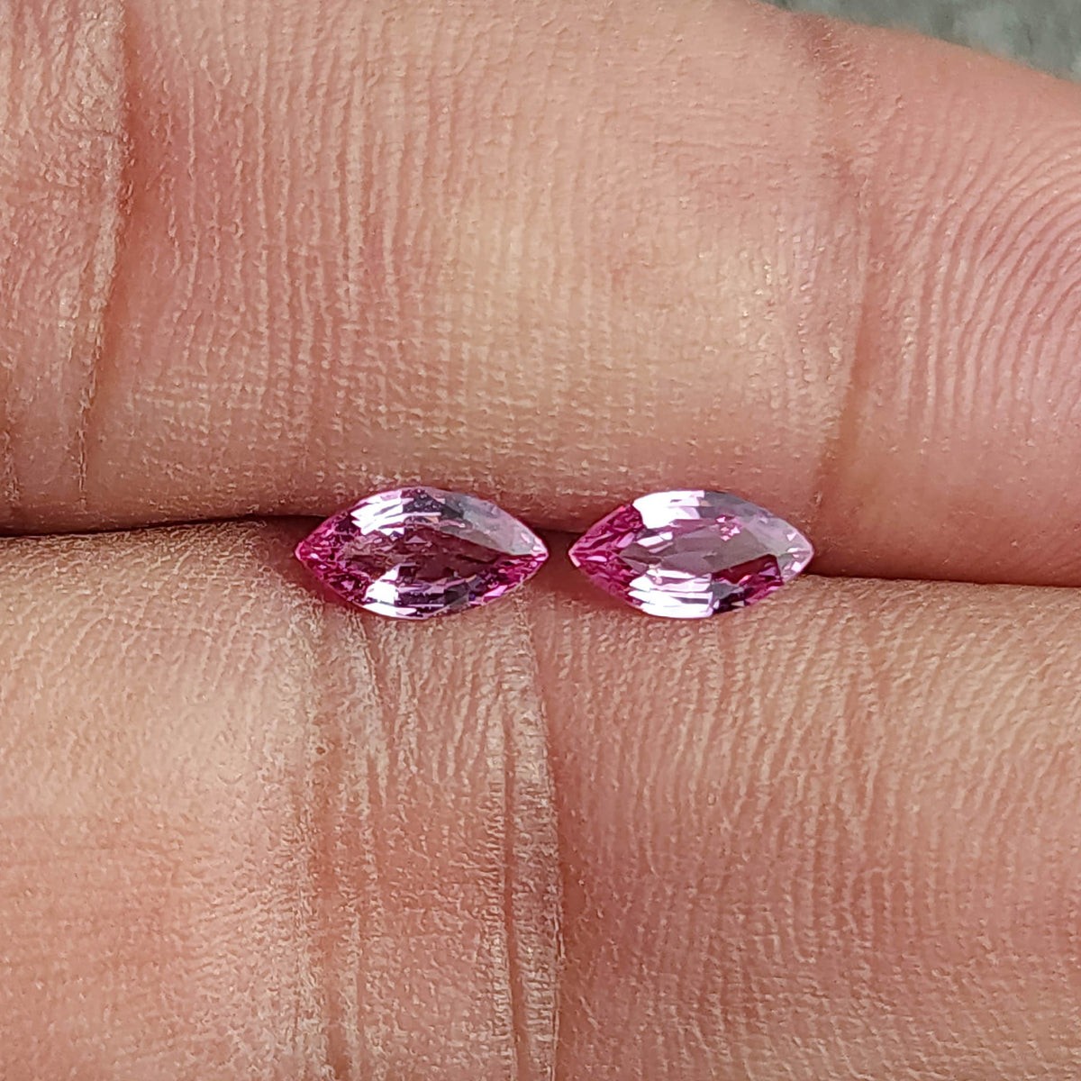 Pink marquise sapphire pair resting side by side between fingertips for a scale reference.