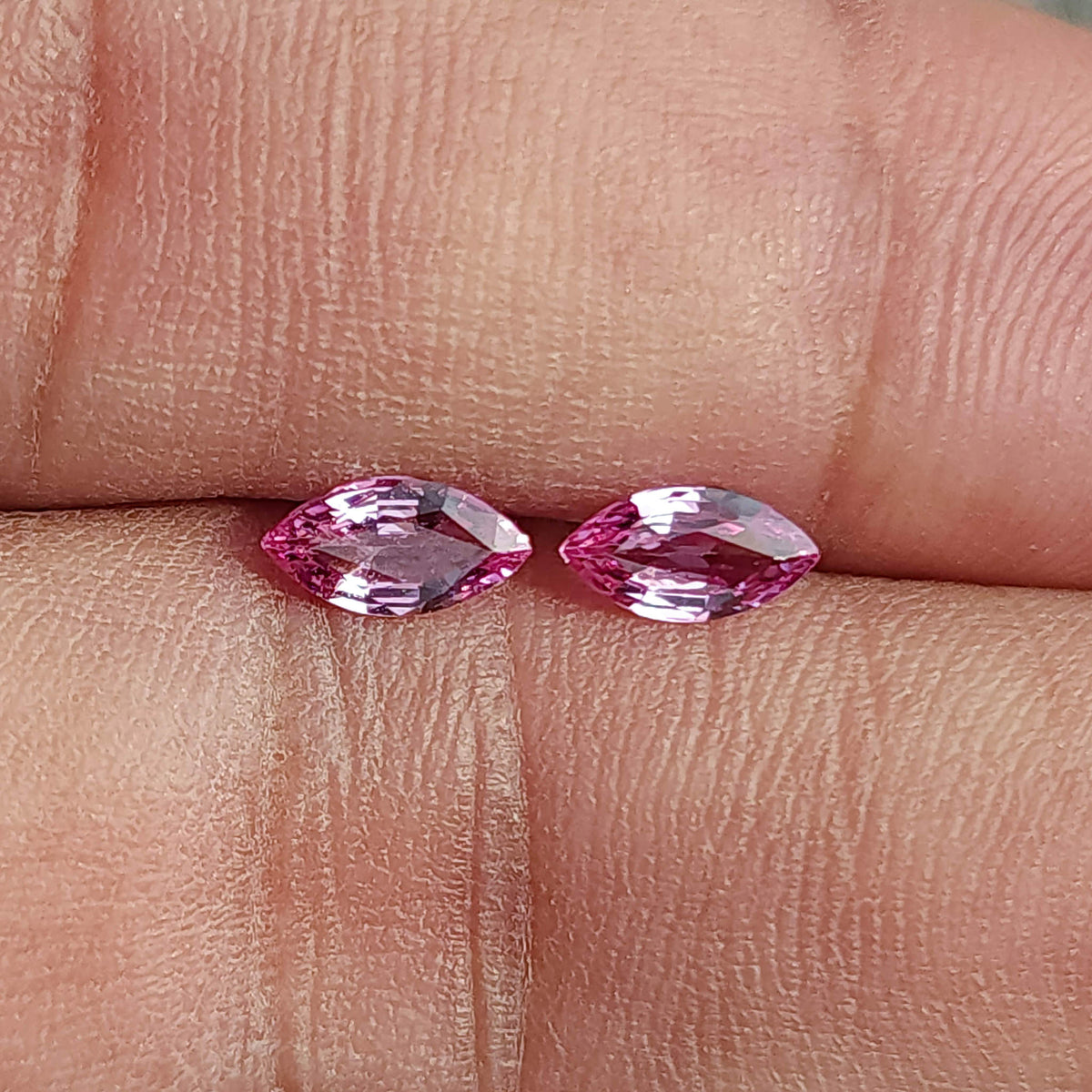 Close face-up view of both pink marquise sapphires between fingertips, with their pointed tips visible.