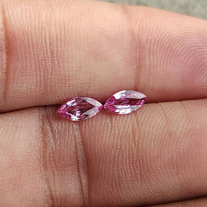 The sapphire pair viewed at a slight angle between fingertips, showing pink and pale facet reflections.