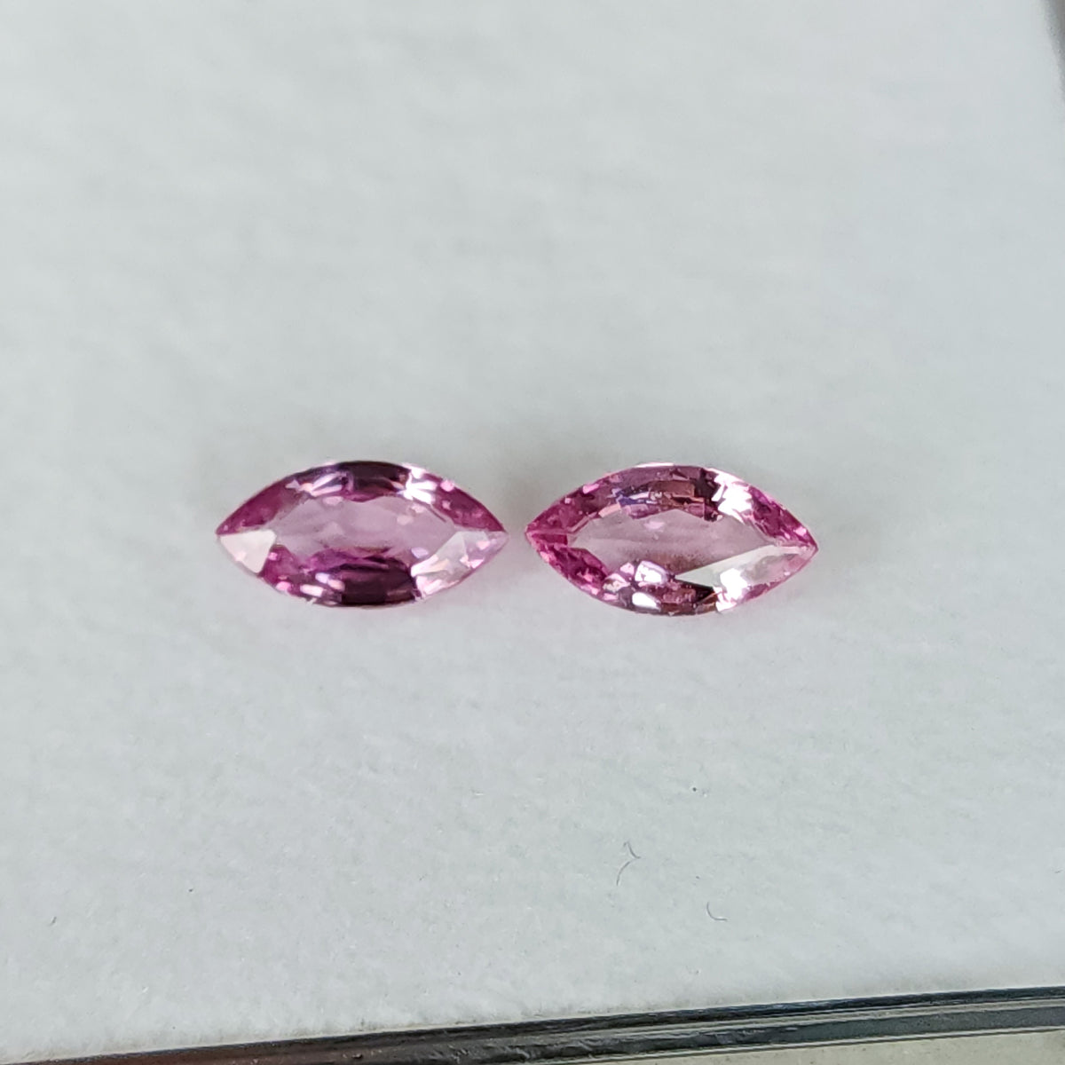 Two pink marquise sapphires arranged horizontally face-up on a plain white tray, with its edge visible below.