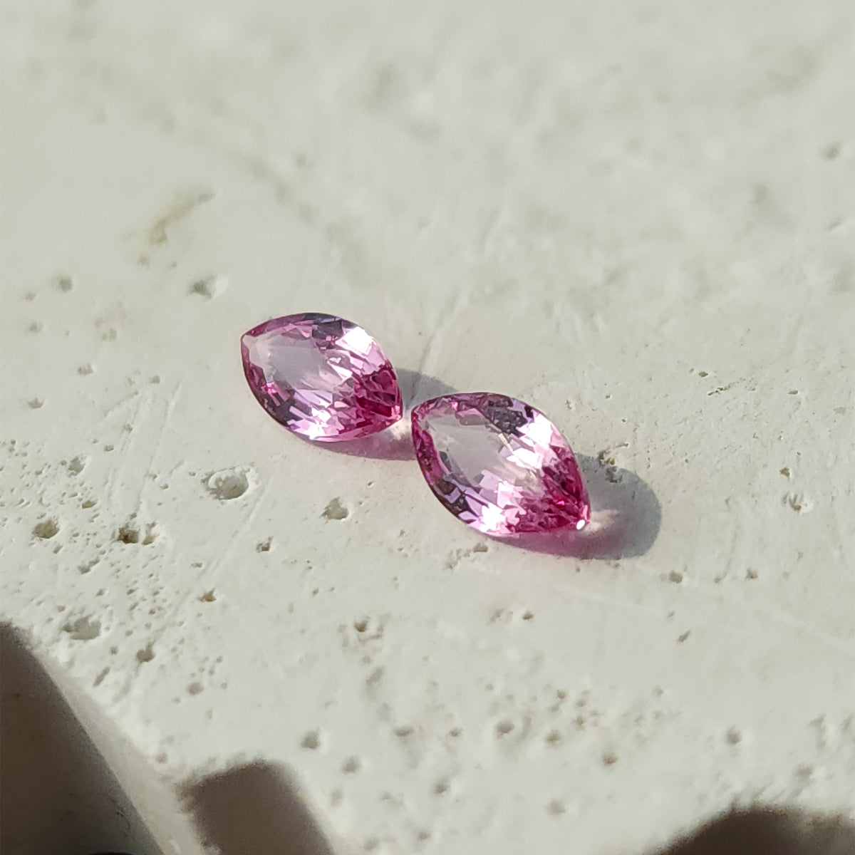 The two pink marquise sapphires at a diagonal angle on a textured white surface.