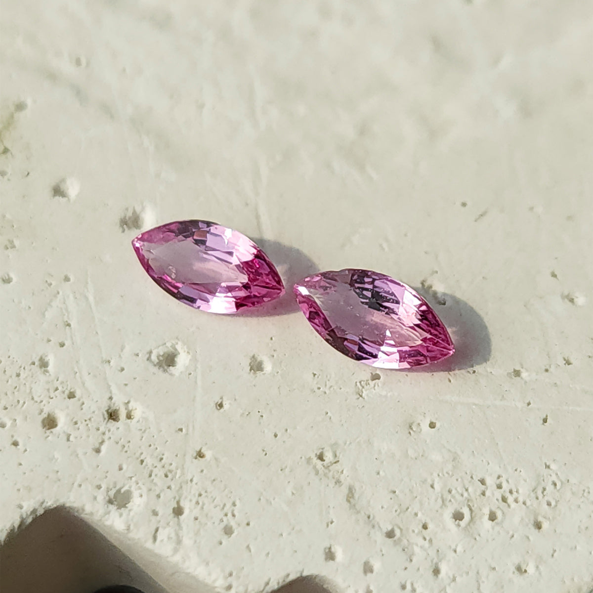 Closer tilted view of the sapphire pair on a textured white surface, showing different facet reflections.