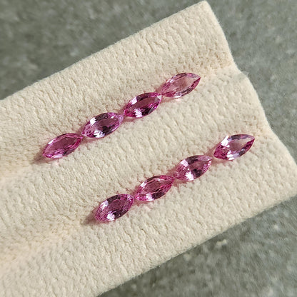 Eight pink marquise sapphires arranged diagonally in two rows of four on a grooved cream display pad.
