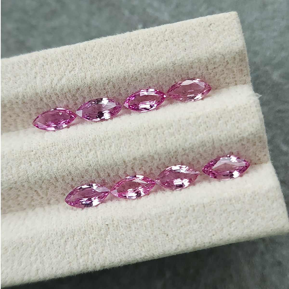 Eight pink marquise sapphires in two rows from a lower angle, with bright reflections across their facets.