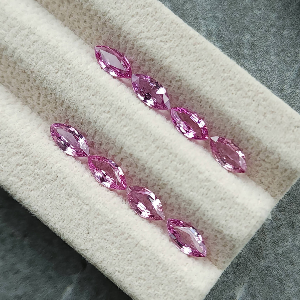 Eight marquise sapphires viewed diagonally on the cream display pad, showing alternating pink and pale facets.