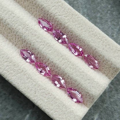 Eight marquise sapphires viewed diagonally on the cream display pad, showing alternating pink and pale facets.