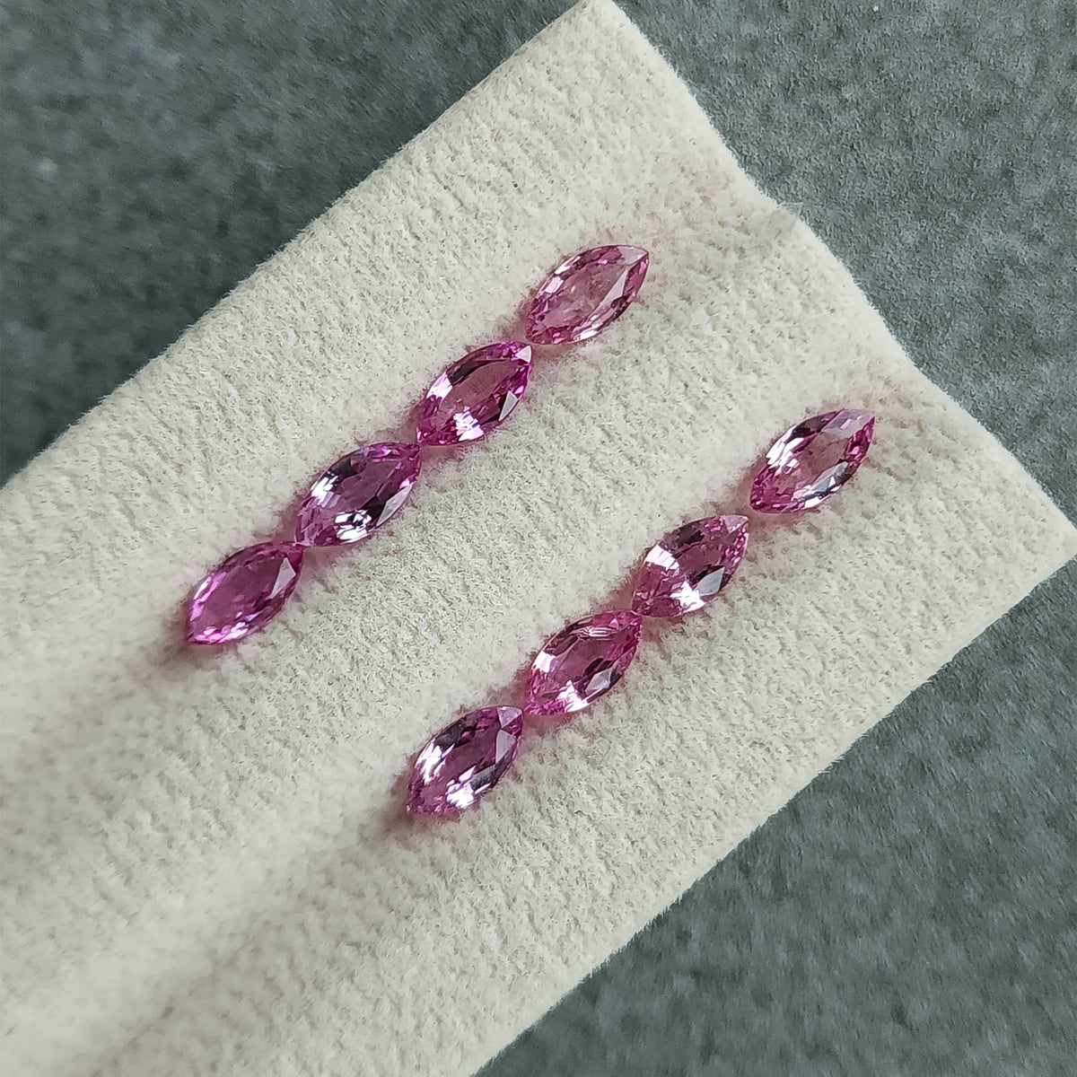 Wider diagonal view of all eight pink marquise sapphires on their grooved cream pad.