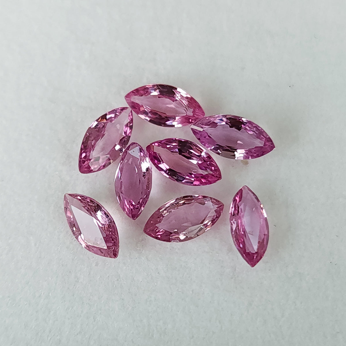 All eight pink marquise sapphires grouped loosely face-up on a plain white tray.