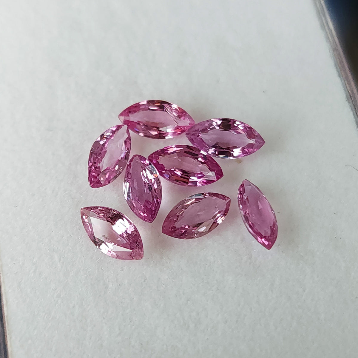 Alternate face-up view of the eight loose marquise sapphires, with mixed pink and pale facet reflections.