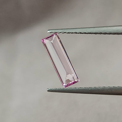 Pink baguette sapphire rotated toward an upright position in tweezers, with a broad pale central reflection.