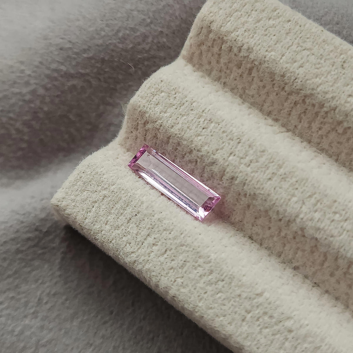 Wider view of the pink baguette sapphire lying on the grooved cream display pad.