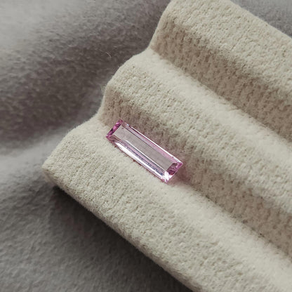 Wider view of the pink baguette sapphire lying on the grooved cream display pad.