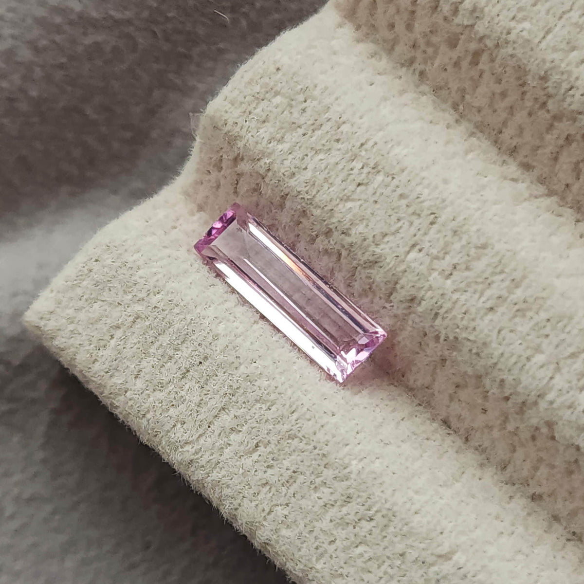 The baguette sapphire viewed diagonally on a cream pad, showing long parallel reflections.