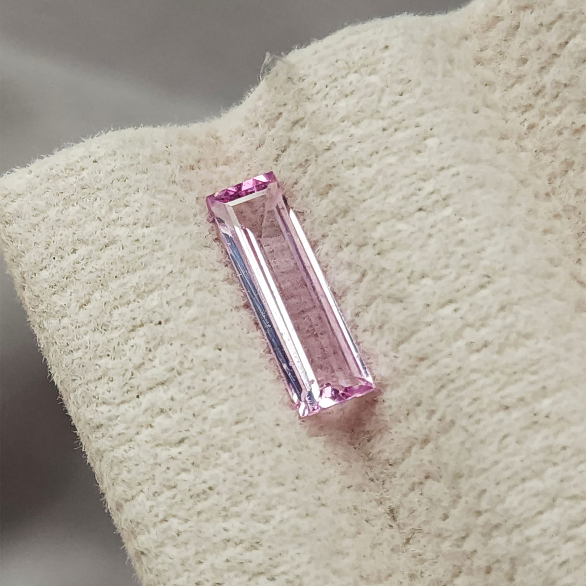 Pink baguette sapphire oriented almost vertically on the cream display pad.