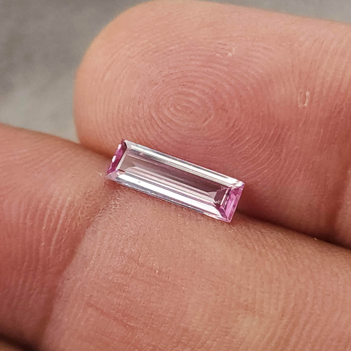 Closer alternate fingertip view of the pink baguette sapphire, with the rectangular step facets visible.