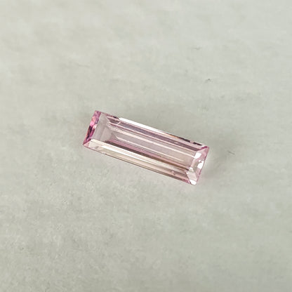 Pink baguette sapphire lying face-up on a white pad, with long pale reflections across its central facets.