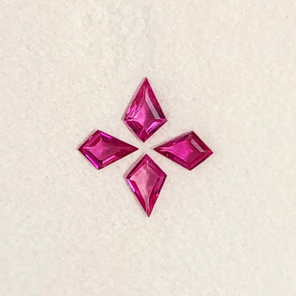 Close face-up view of all four fuchsia pink kite rubies, with their points facing outward on a white pad.