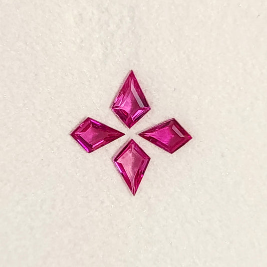Close face-up view of all four fuchsia pink kite rubies, with their points facing outward on a white pad.