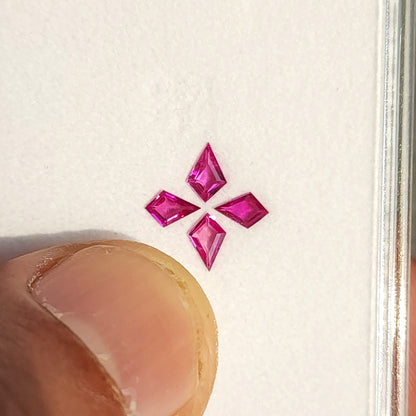 Four pink kite rubies beside a thumb on their white display tray for a scale reference.