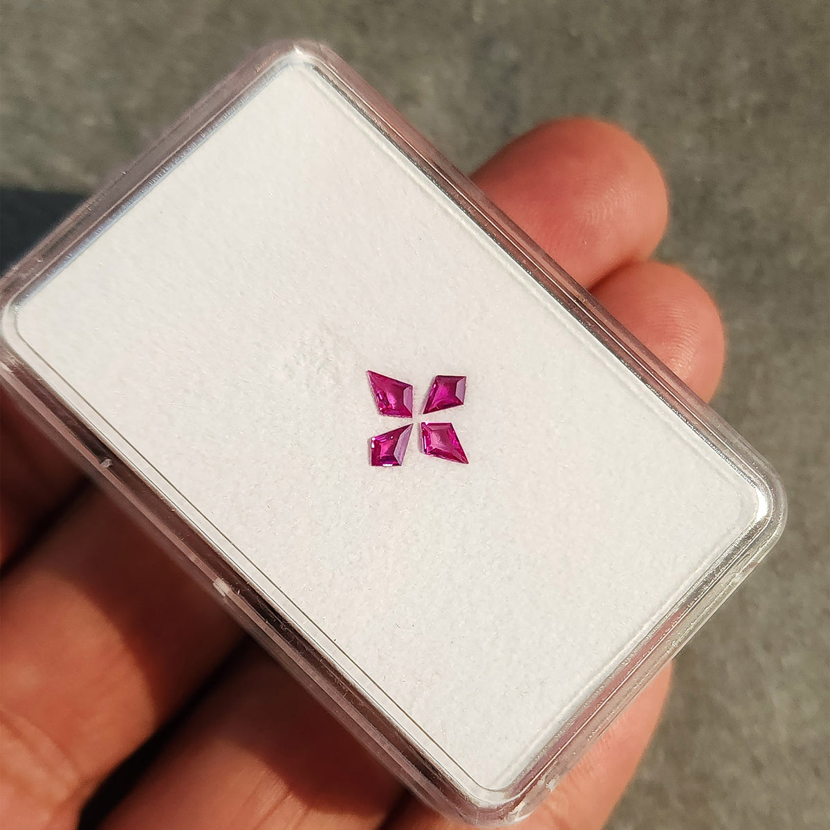 White ruby display tray held diagonally in a hand, with the complete four-stone cross visible.
