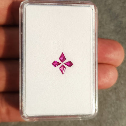 Full white tray held vertically in a hand, containing the four pink kite rubies.