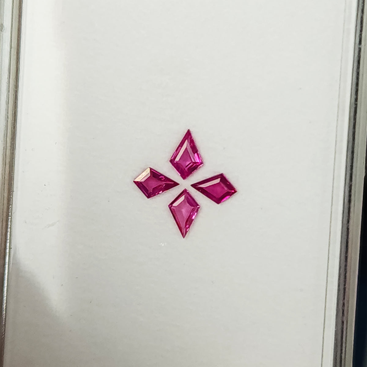The four-ruby arrangement at a tilted tray angle, showing pale reflections across some pink facets.