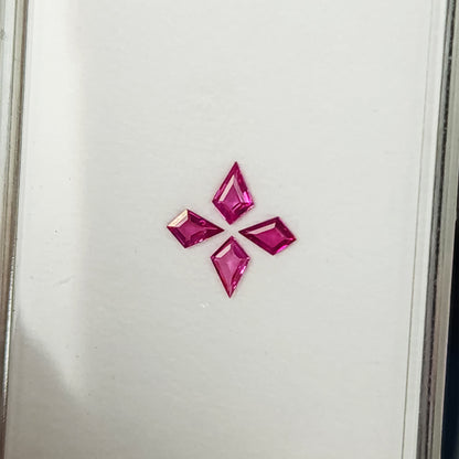 The four-ruby arrangement at a tilted tray angle, showing pale reflections across some pink facets.