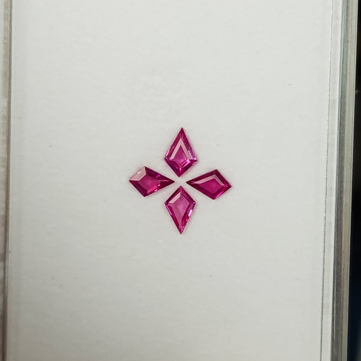 Wider face-up view of the complete four-kite ruby set near the lower portion of the white tray.