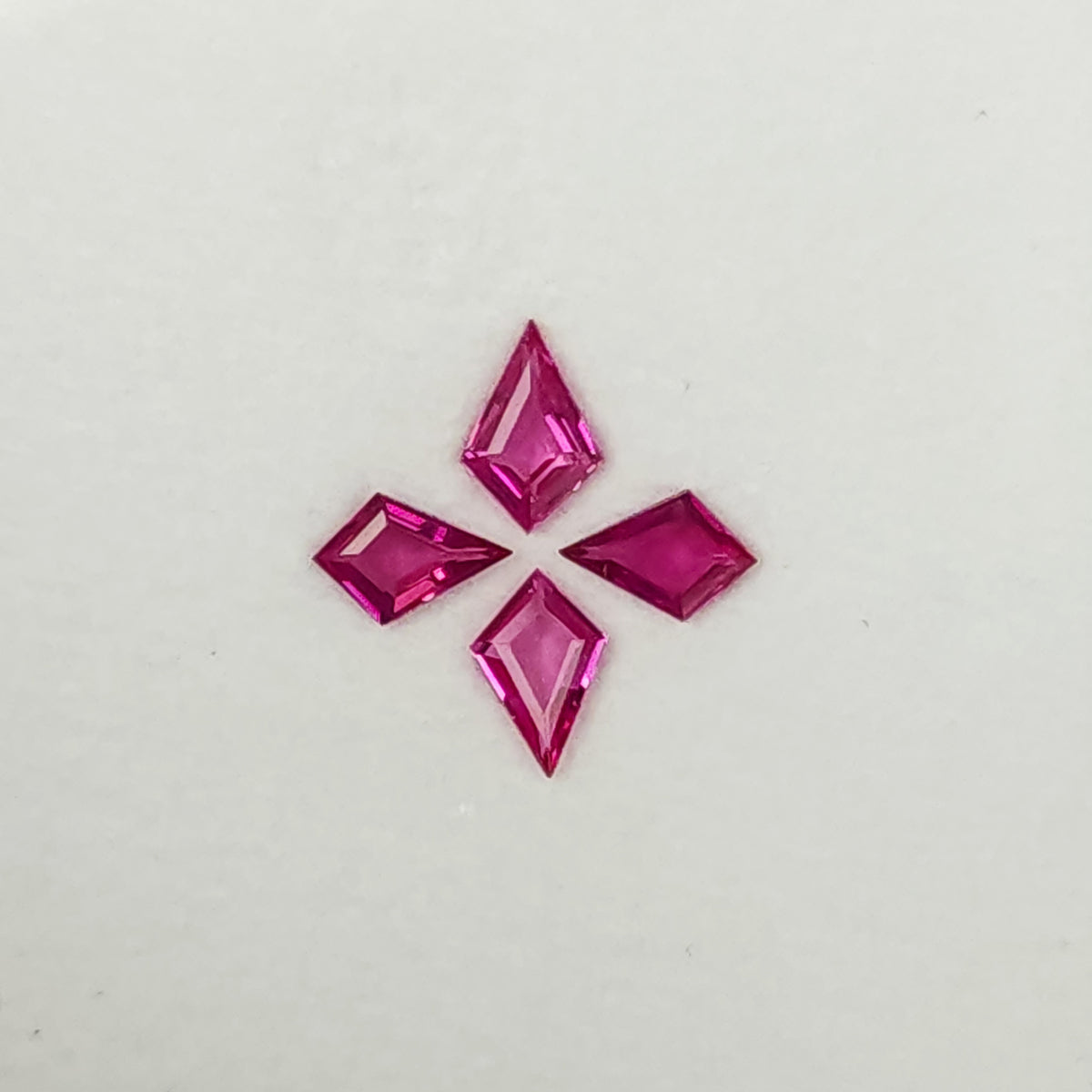 Close alternate face-up view of the four pink kite rubies, showing their central facets and varied outlines.