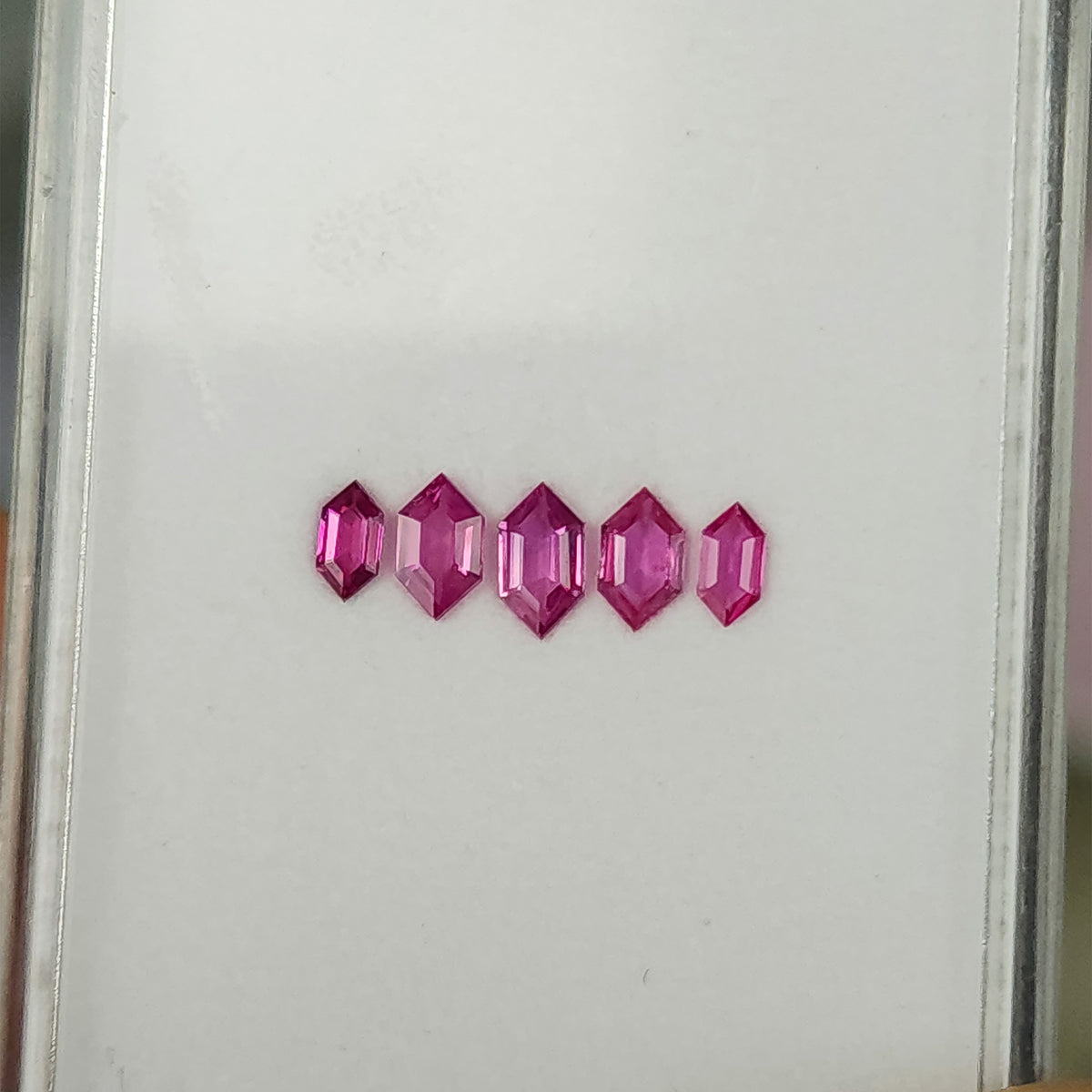 Wider white-tray view of the complete five-ruby parcel.