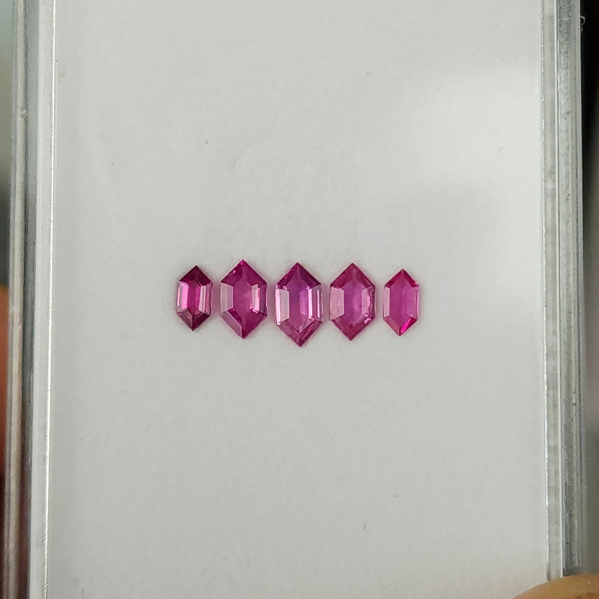 Five pink rubies in a horizontal row on a white tray, showing their different sizes.