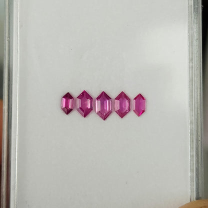 Five pink rubies in a horizontal row on a white tray, showing their different sizes.