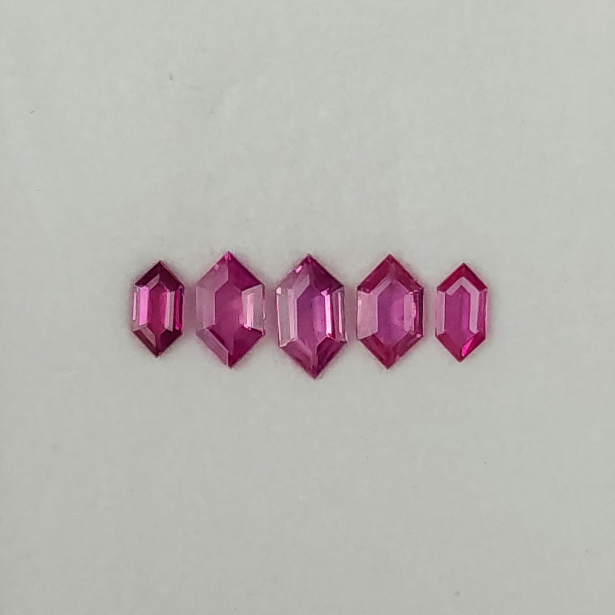 Five raspberry-pink geometric rubies arranged face-up in a row, with the largest at the center.