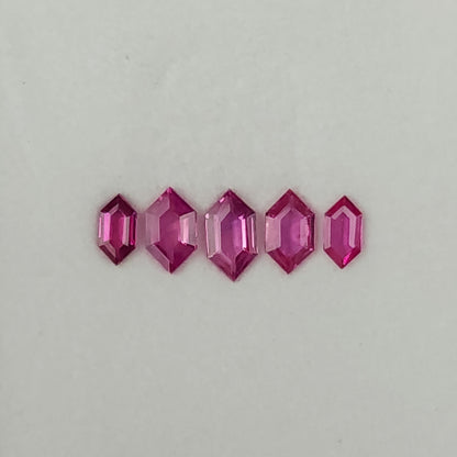 Five raspberry-pink geometric rubies arranged face-up in a row, with the largest at the center.