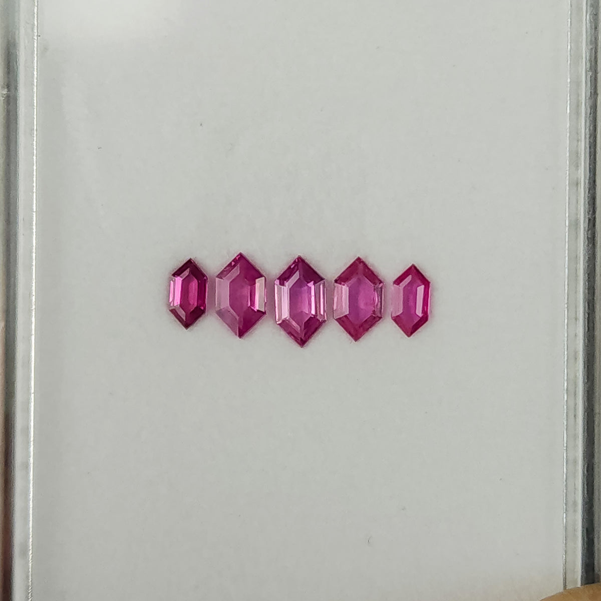The five pink rubies tilted in a row, with brighter reflections on their facets.