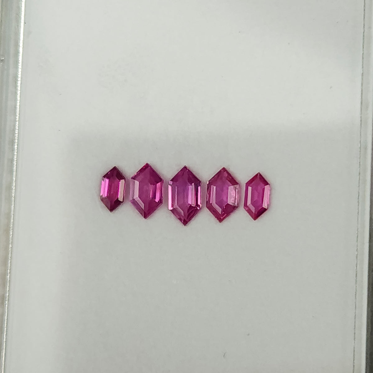 Five pink rubies viewed from an oblique angle, with their elongated outlines visible.