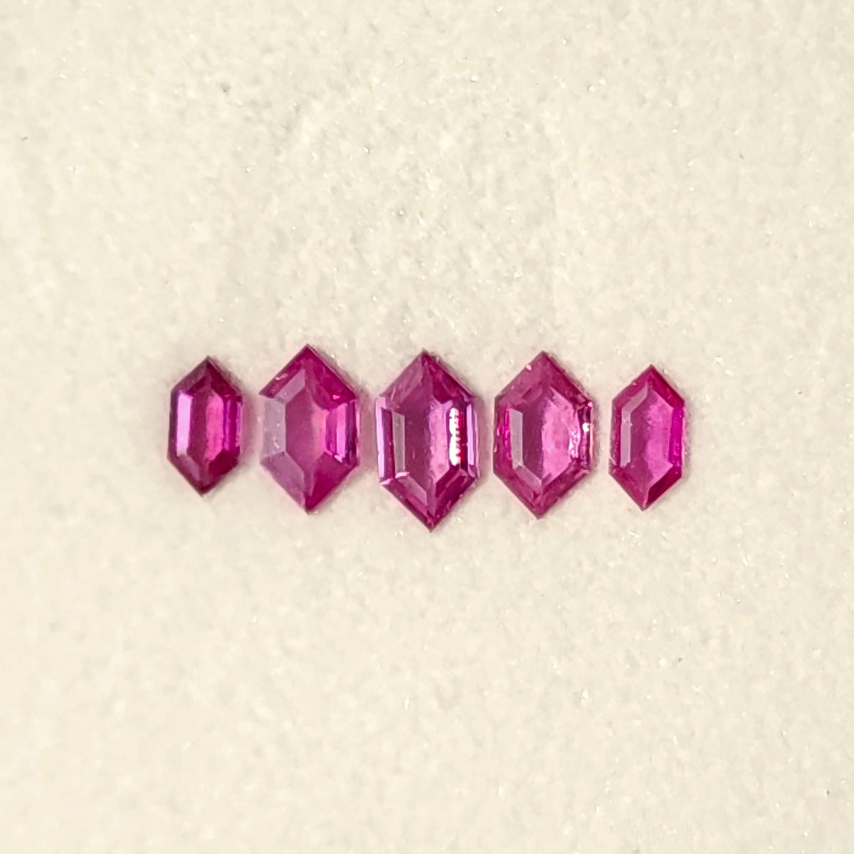 Close white-pad view of the five raspberry-pink rubies, showing the faceted geometric outlines.