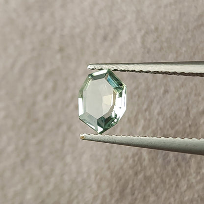 Mint green sapphire tilted slightly in tweezers, with light reflected across its central table.