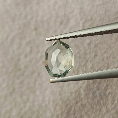 Mint green sapphire rotated in tweezers to show broader reflective facets.