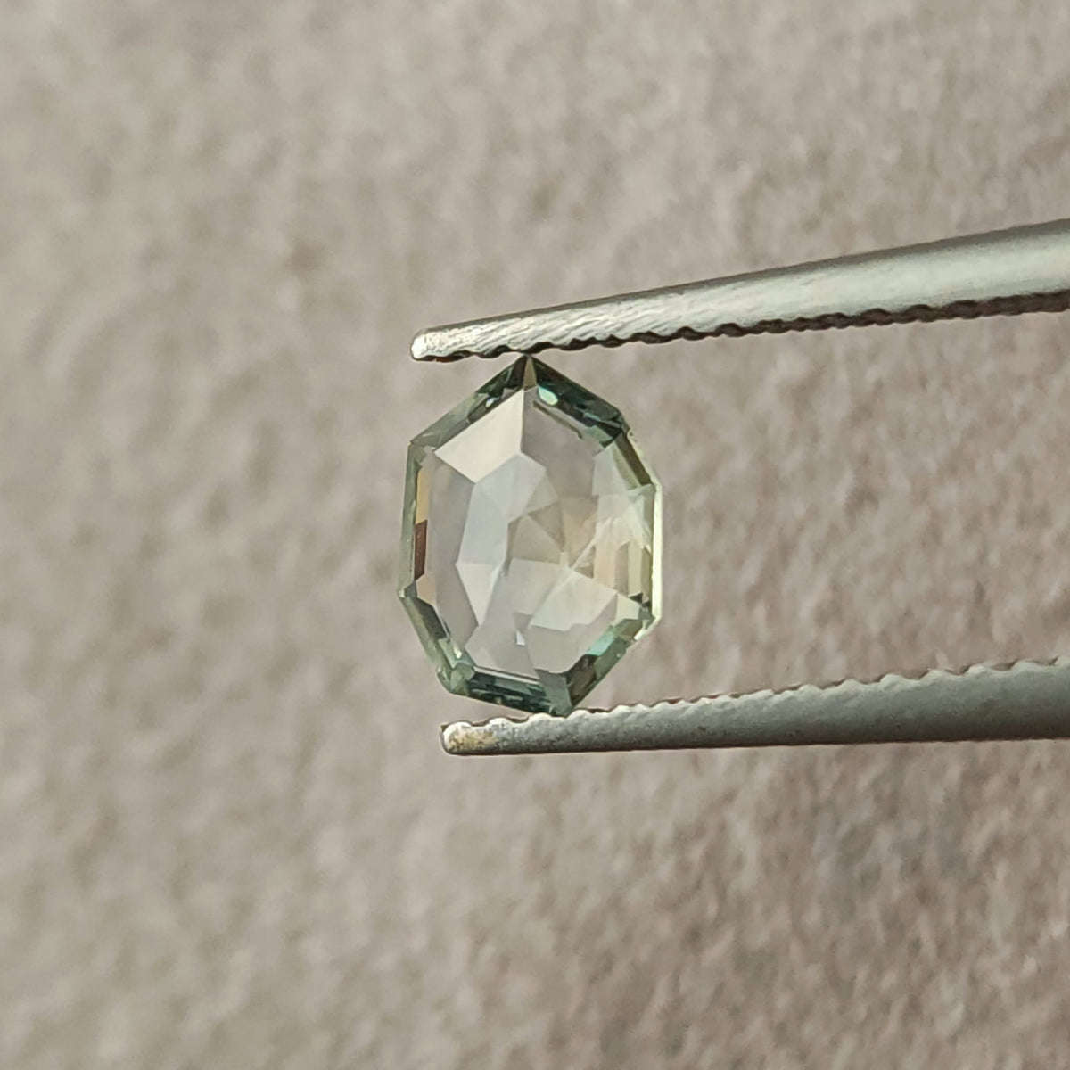Mint green sapphire at an alternate tilted angle in tweezers, with pale reflections.