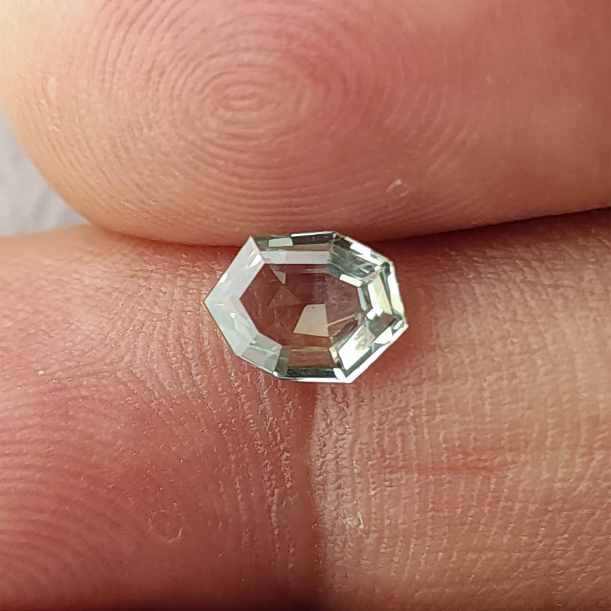 Mint green octagonal sapphire between two fingertips for scale, viewed face-up.