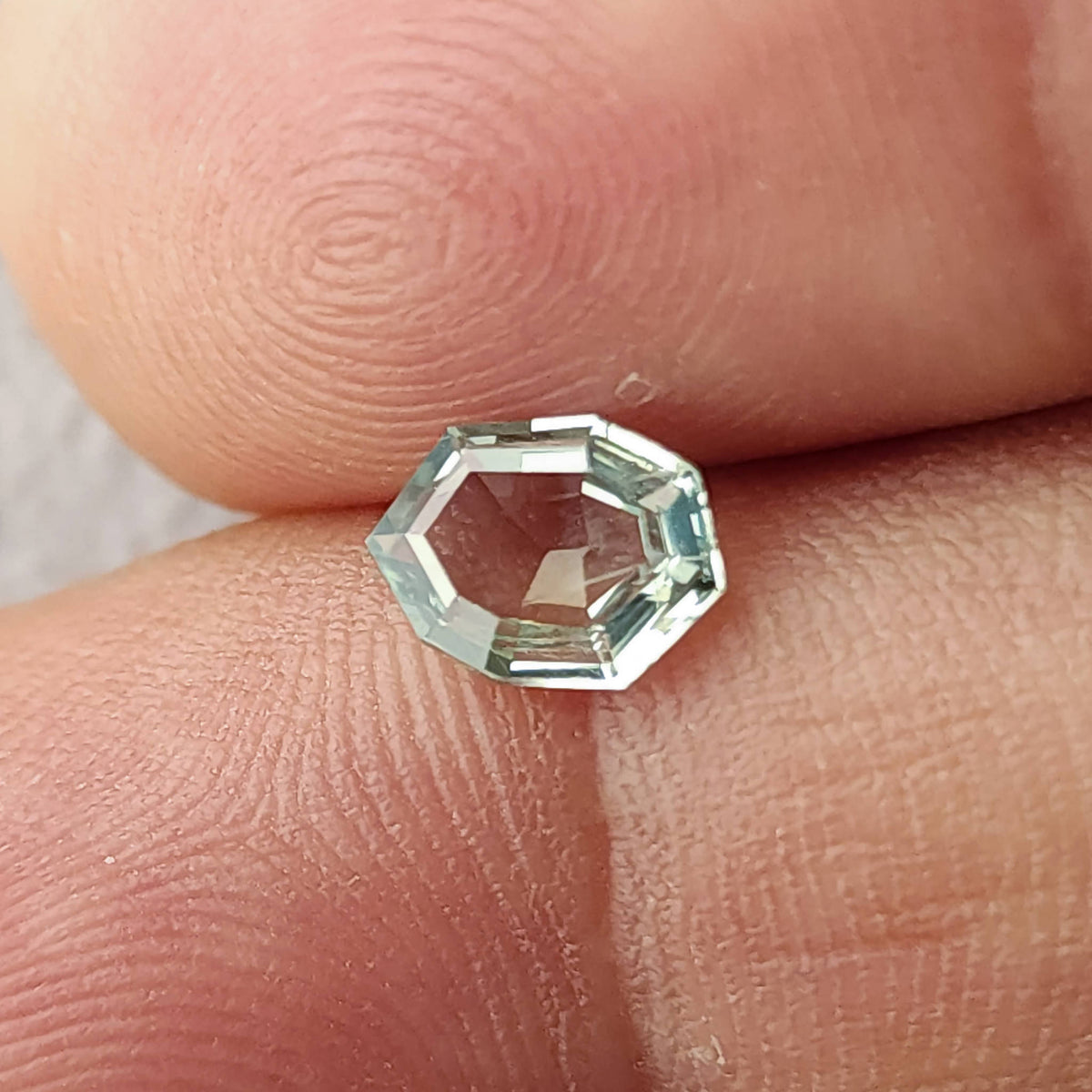 Mint green sapphire tilted between fingertips, showing reflective step facets.