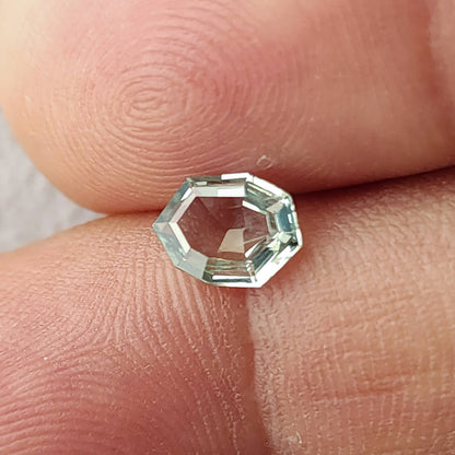 Mint green sapphire tilted between fingertips, showing reflective step facets.