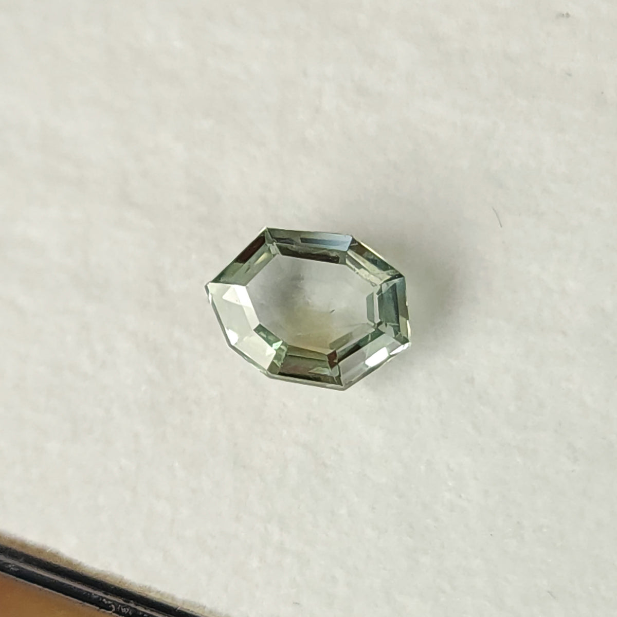 Mint green sapphire face-up on a white pad, showing its eight-sided outline and step facets.