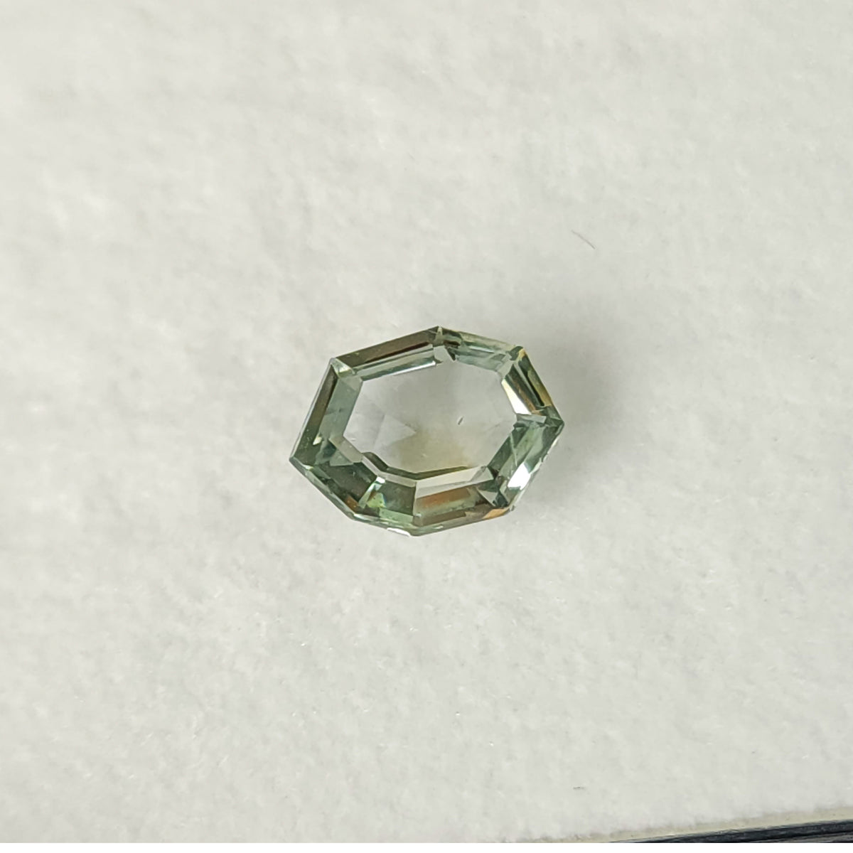 Mint green sapphire on a white pad from a lower oblique angle, with the outline visible.