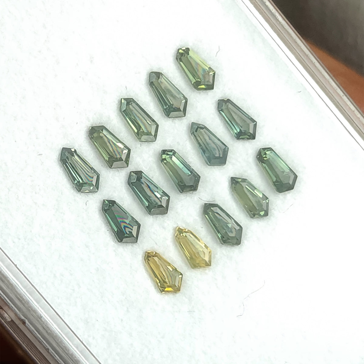 Tilted sapphire tray with brighter pale reflections across some green stones.