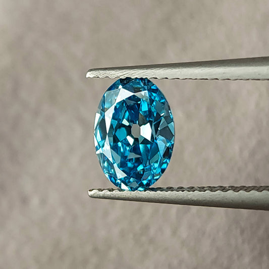 Blue oval diamond held face-up in tweezers, showing broad facets and the oval outline.