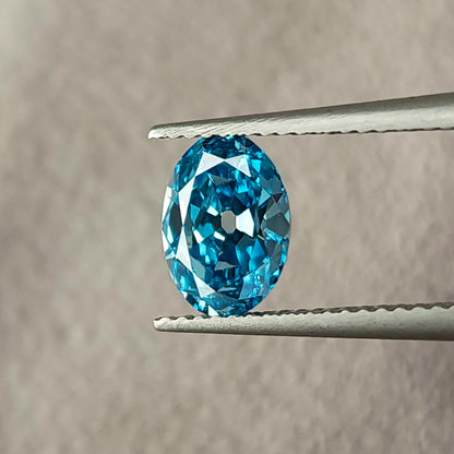 Blue oval diamond at a slightly different face-up angle in tweezers.