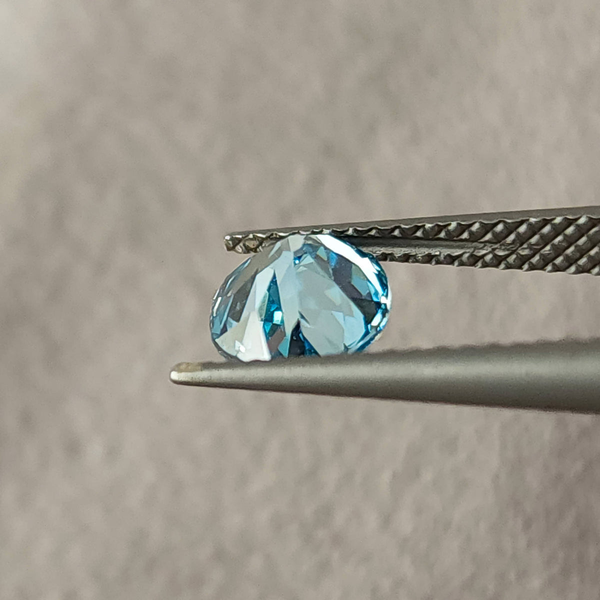 Side view of the blue oval diamond held between tweezers, showing its depth profile.